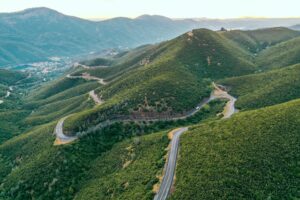 An aerial shot of beautiful green hills and mountains with a narrow curvy road in the middle