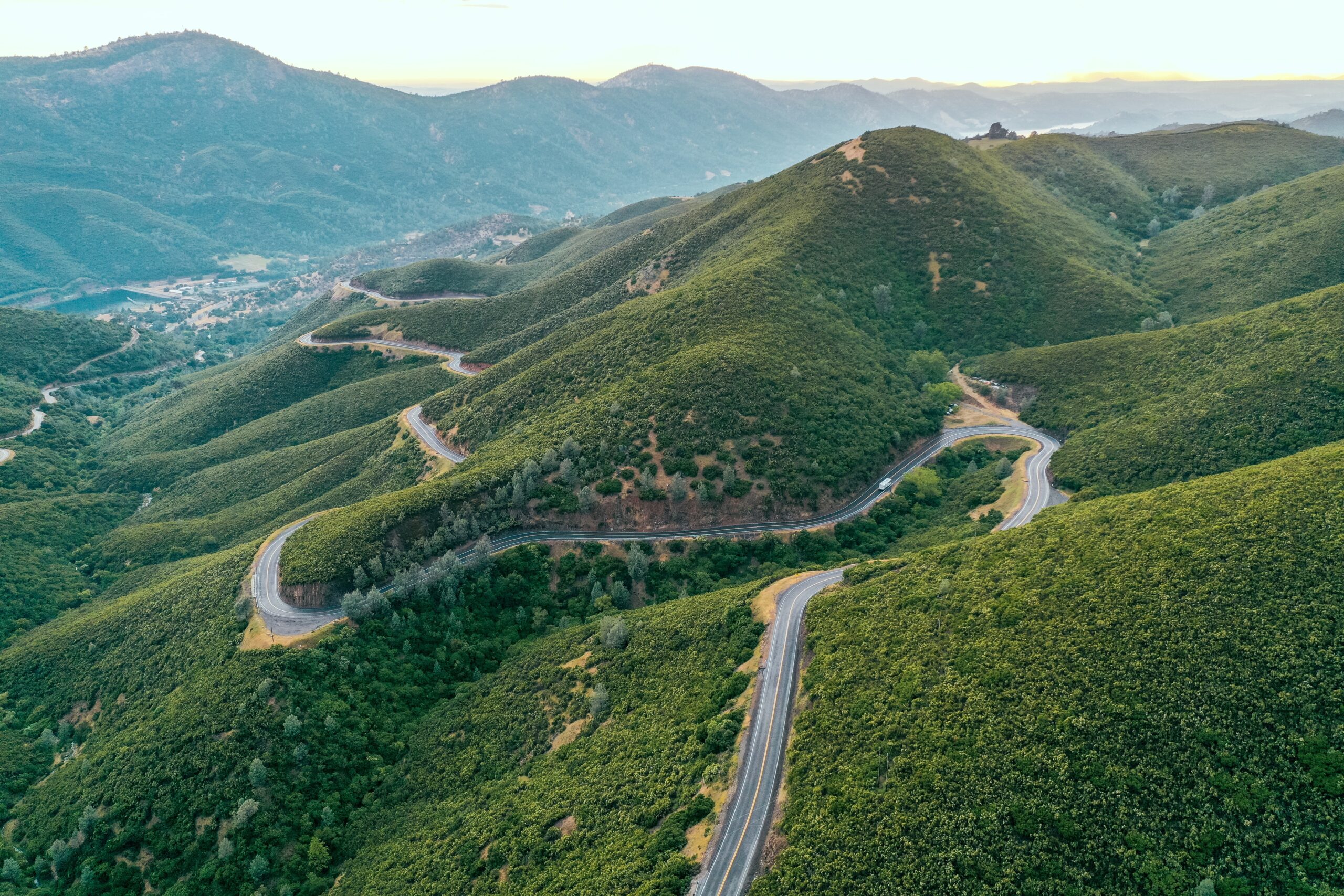 An aerial shot of beautiful green hills and mountains with a narrow curvy road in the middle