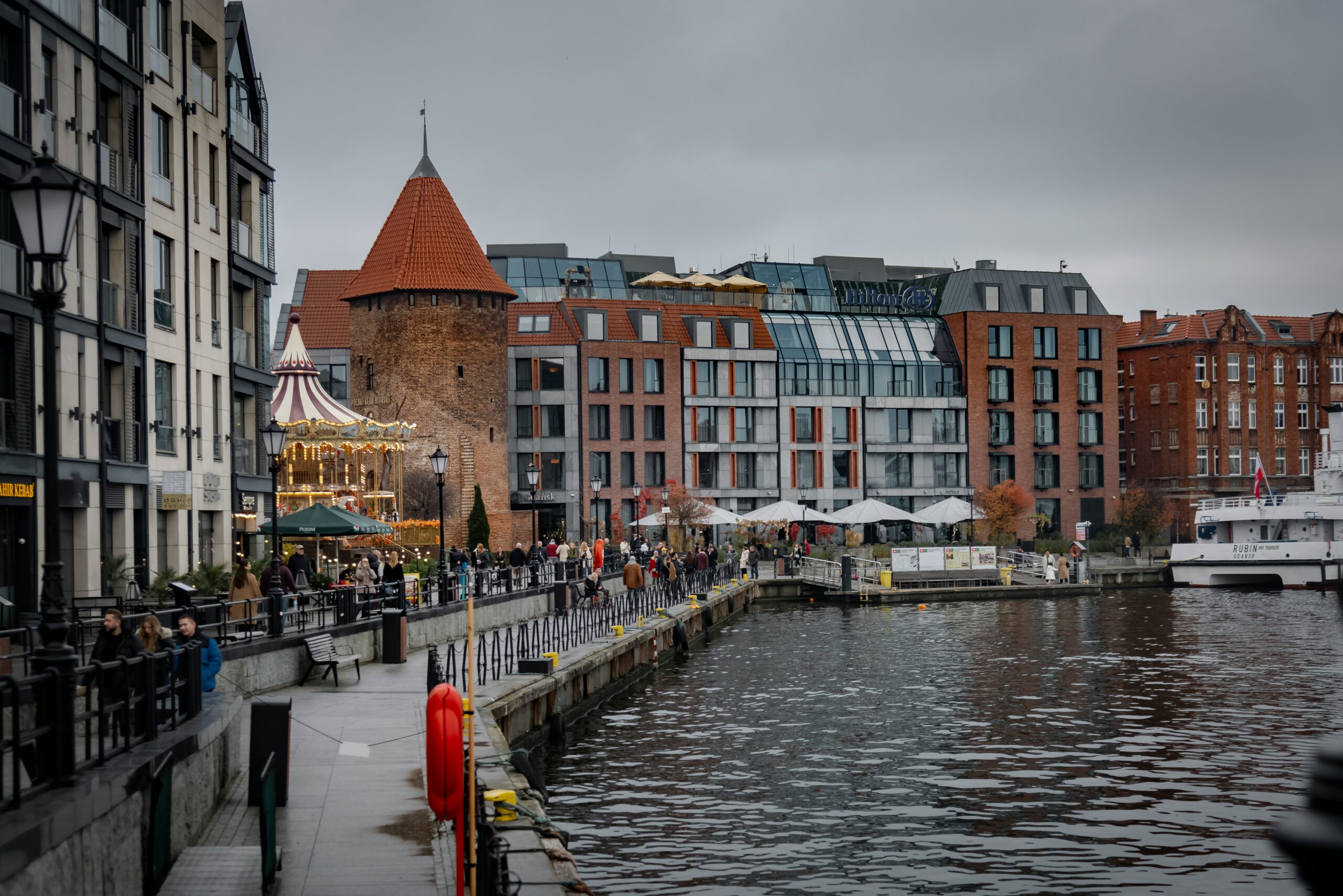 Waterfront buildings with a carousel and people walking in Gdansk in Poland.